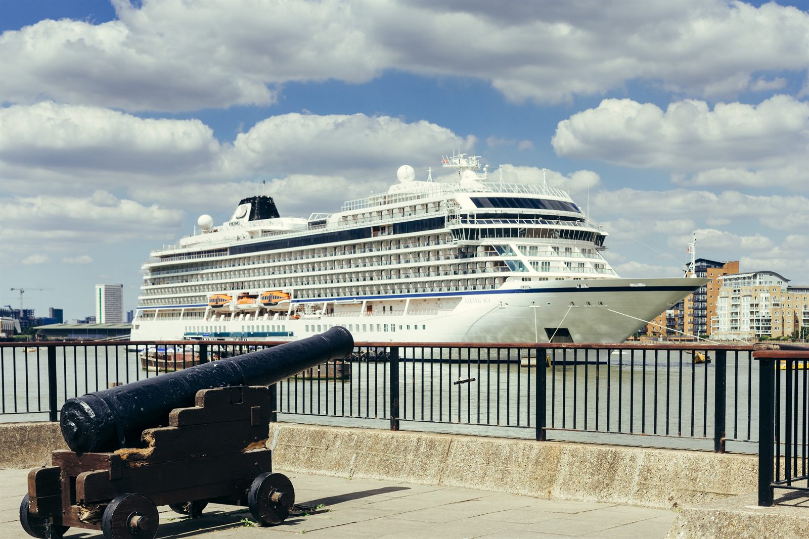 Ocean cruise ship moored on a city river quay beside an old cannon