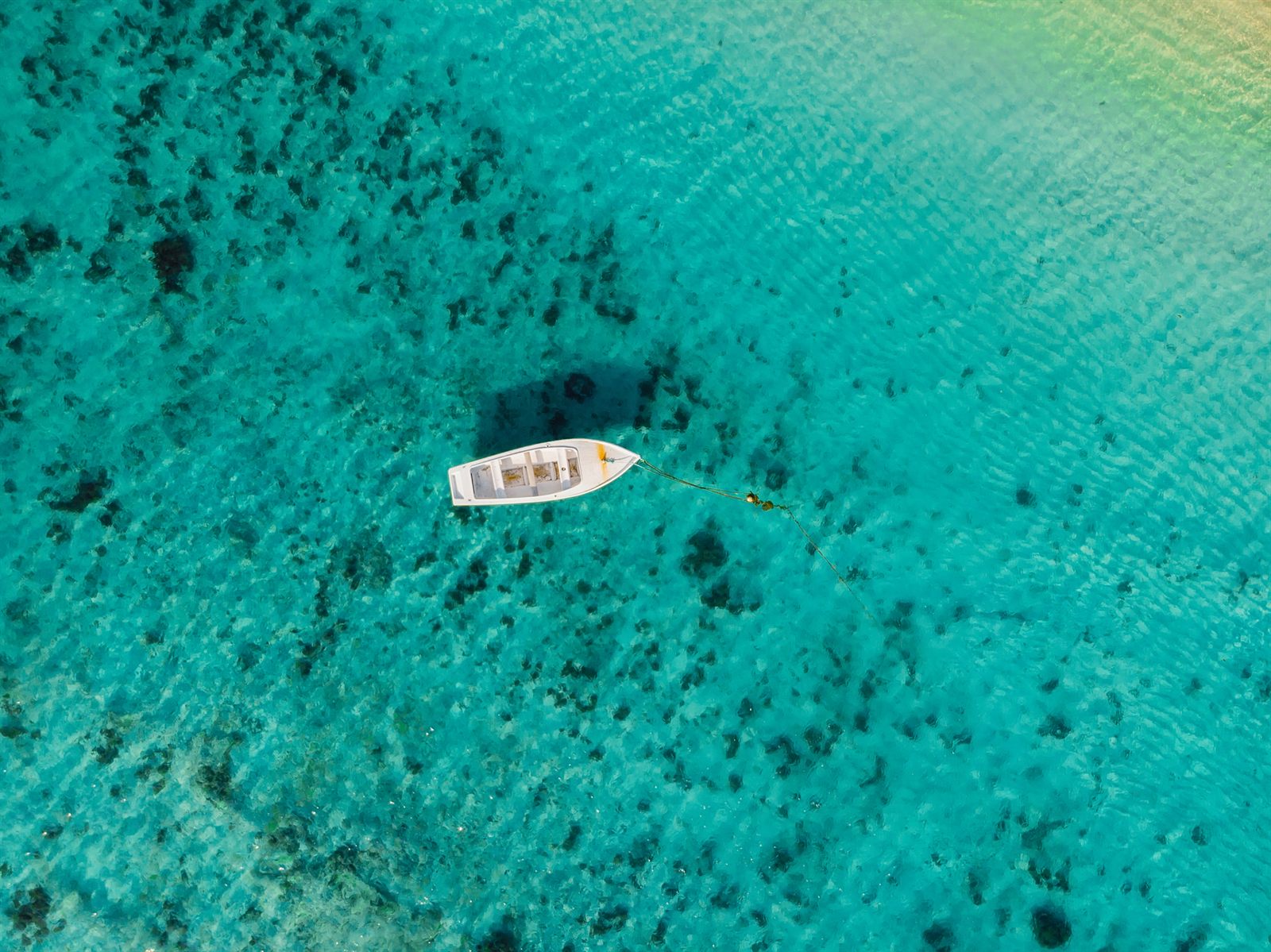 Small boat floating on clear turquoise Caribbean water seen from above